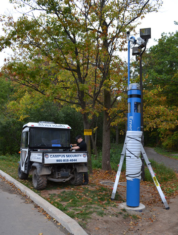 David Perreault, Sheridan's security operations coordinator, puts the finishing touches on one of the new emergency stations installed next to the forest bordering the college's Trafalgar Campus. (Chris Coutts / The Sheridan Sun)