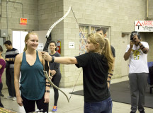 A trainer helps out a player learning how to shoot the bow.
