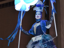 A woman dressed in blue and white twirls around on the glowing purple stage with her lantern. 